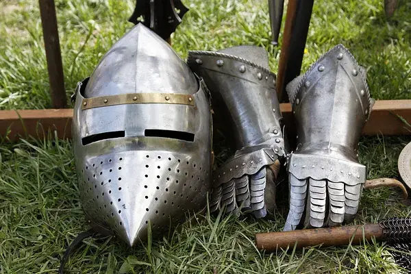 Medieval knight's helmet and gauntlets resting on grass, symbolizing protection and resistance