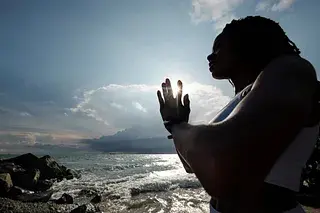 Black woman standing in prayer by the ocean, symbolizing self-compassion and inner strength amid uncertainty