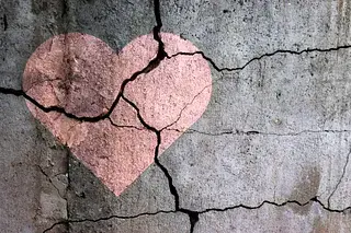 Faded heart painted on a cracked concrete wall, symbolizing emotional strain and societal damage under authoritarian systems