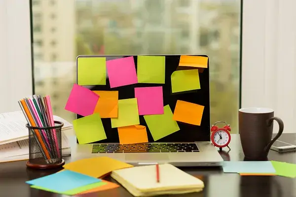 Laptop covered in colorful sticky notes on a busy desk, representing creative brainstorming and organized planning.