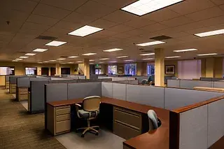 Rows of empty cubicles in a dimly lit federal office, symbolizing the threat to public servants and democratic institutions