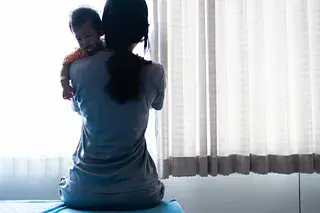 Silhouette of a mother holding a baby near a window, symbolizing hidden harm and vulnerability of children