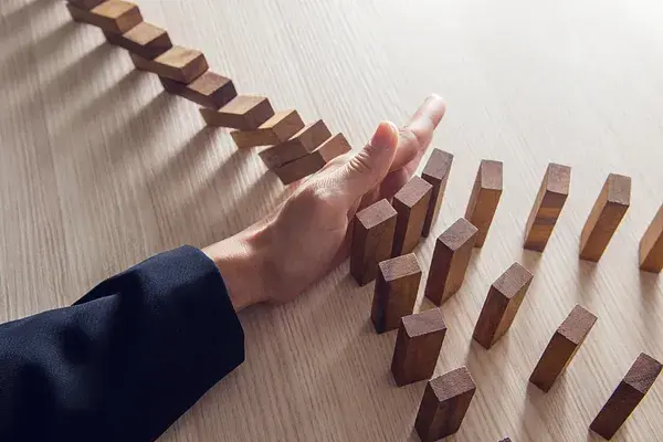 A hand stopping falling dominoes on a wooden table, symbolizing interrupting cycles of panic and reclaiming control